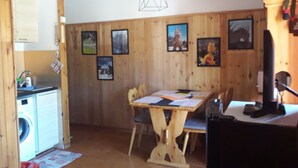 A wooden interior with a dining table, chairs, a washing machine, and framed pictures on the wall.