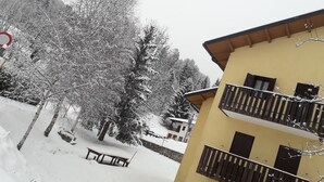 A multi-story building with balconies, a stone wall, and a bench in the snow.