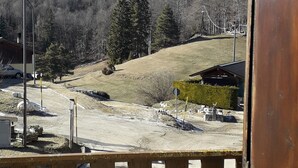A view from a balcony overlooking a construction site with a dirt road, a wooden fence, and a forested hill in the background.