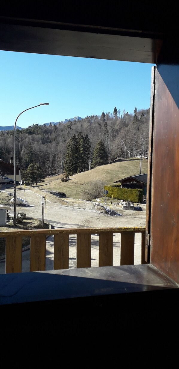 A view from a balcony overlooking a construction site with a dirt road, a wooden fence, and a forested hill in the background.