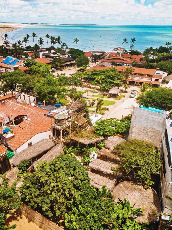 A coastal town with traditional architecture, including thatched-roof structures and red-tiled buildings, surrounded by lush greenery and a beach.