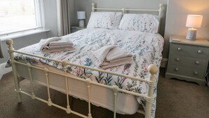 A neatly made bed with floral bedding, a bedside lamp, and a nightstand with a lamp. - 6 Milton Place (Bideford)