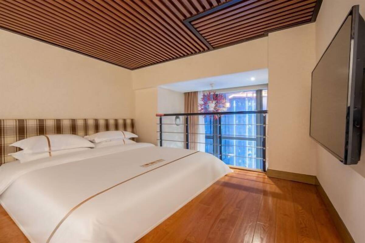 Quarto com uma cama grande, teto de madeira e vista através de uma porta de vidro.