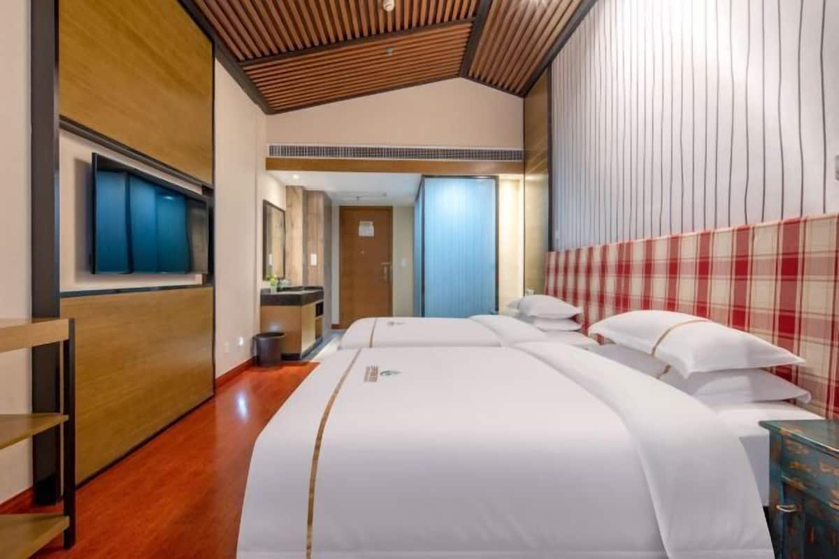 Quarto de hotel com teto de madeira, uma cama grande com roupa de cama branca, televisão na parede e uma parede com padrão xadrez vermelho.