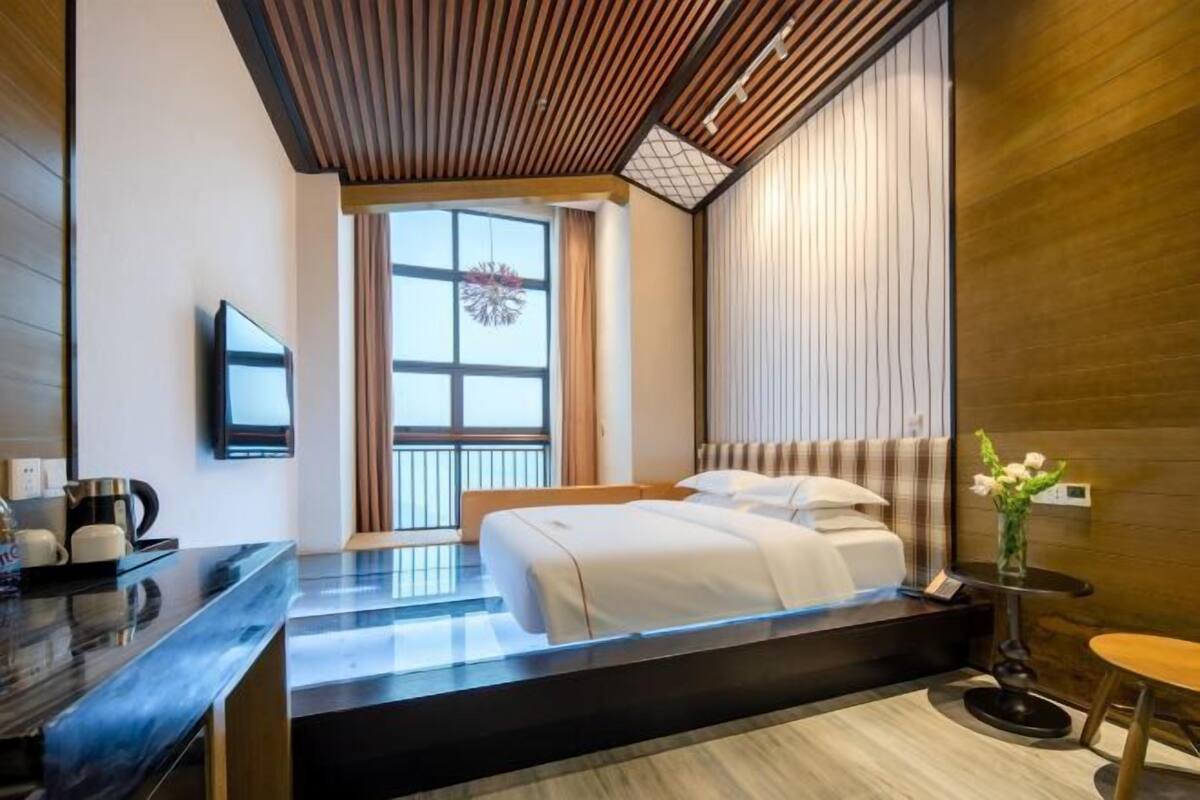 Quarto de hotel moderno com cama, escrivaninha, televisão e janela com cortinas.
