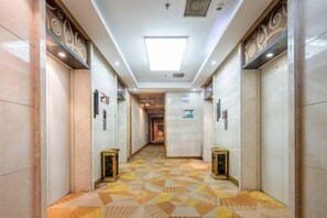 A hotel corridor with a geometric patterned floor, doors on either side, and a central walkway leading to an elevator. - Lanting Wanpan Hotel (Changsha)