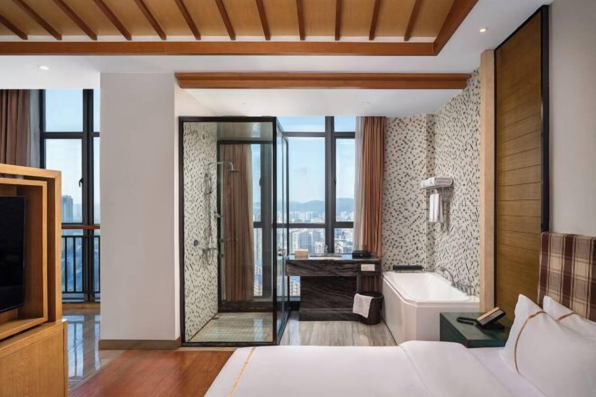 Quarto de hotel com uma cama grande, banheiro com banheira, escrivaninha e televisão.