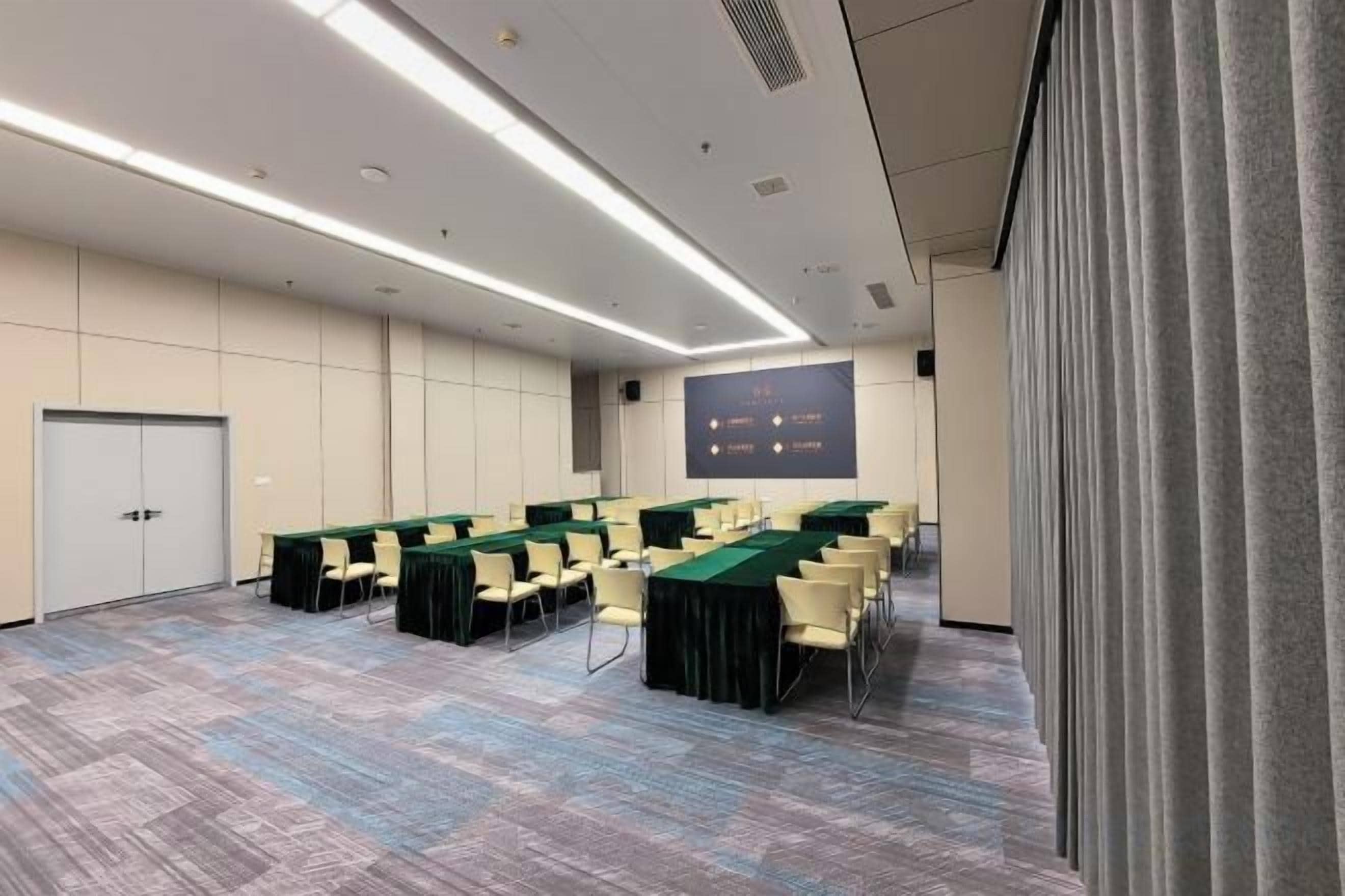 A conference room with a long table, chairs, a projector screen, and a carpeted floor.