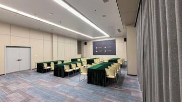 A conference room with a long table, chairs, a projector screen, and a carpeted floor.