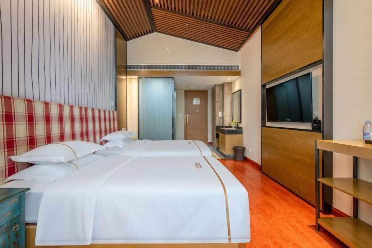 Quarto de hotel com cama, televisão, secretária de madeira e banheiro visível ao fundo.