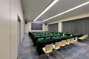 A conference room with rows of tables and chairs, a projector screen, and a large window with curtains.