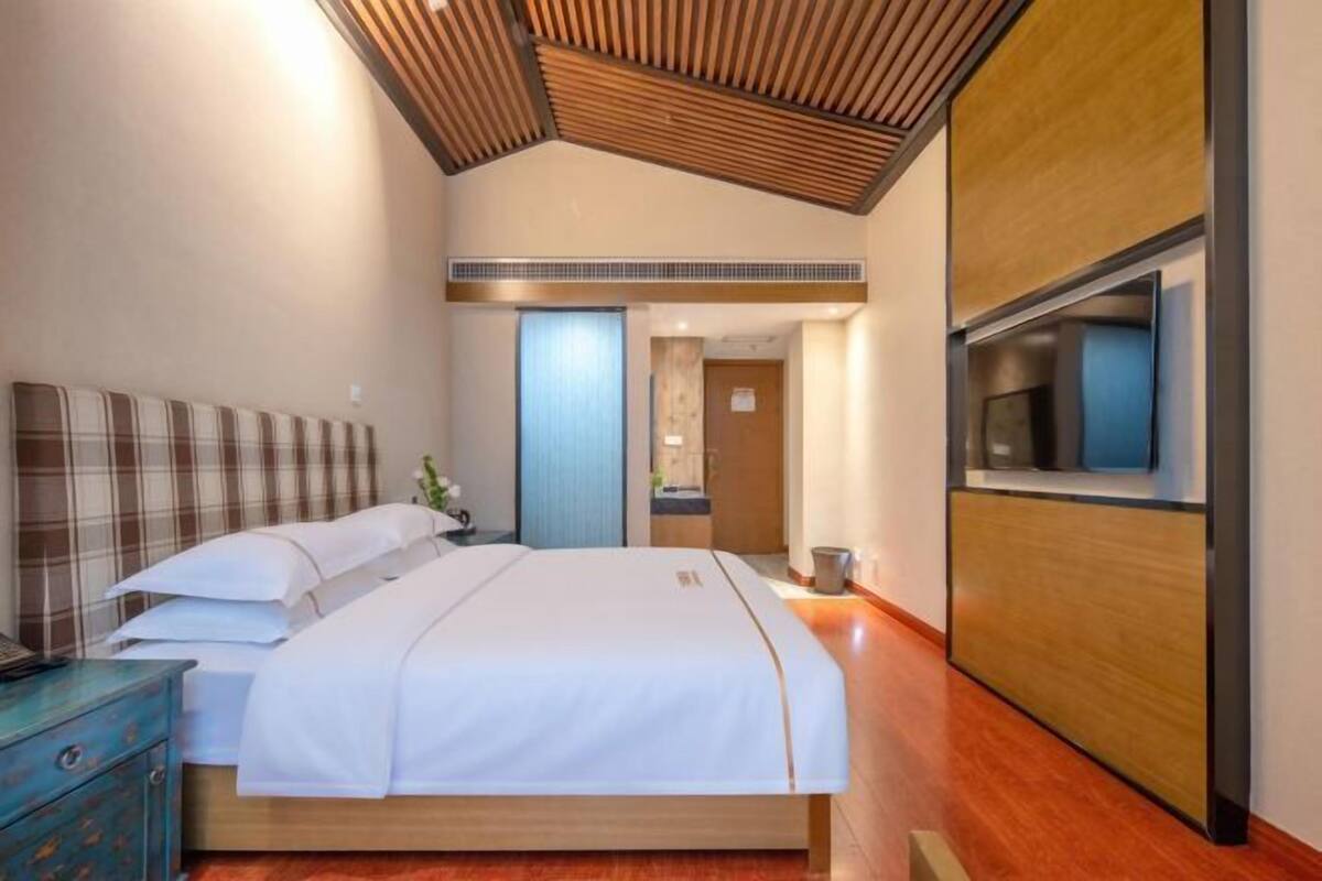 Quarto de hotel moderno com uma cama grande, teto de madeira e uma janela ampla.