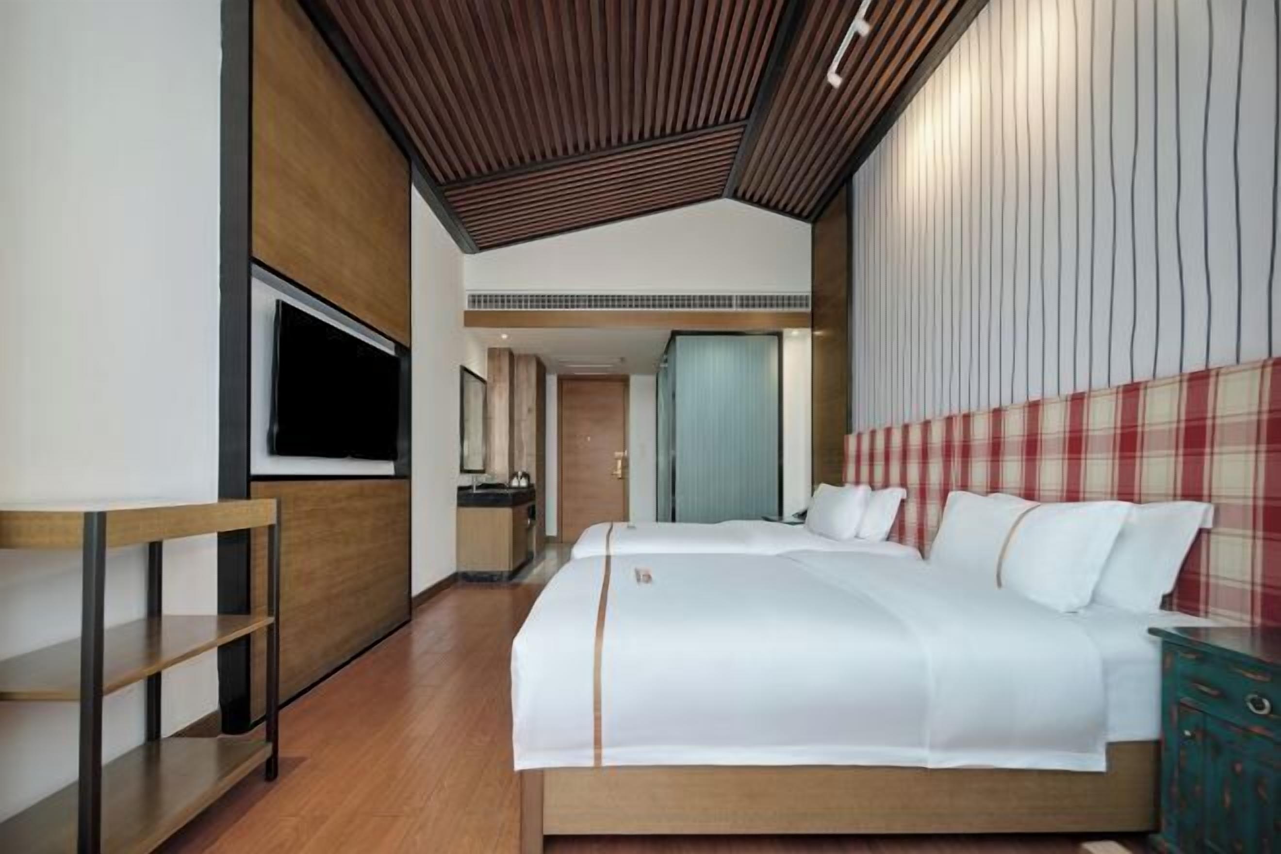 A modern hotel room with a large bed, a TV, a wooden desk, and a wardrobe.