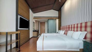 A modern hotel room with a large bed, a TV, a wooden desk, and a wardrobe.