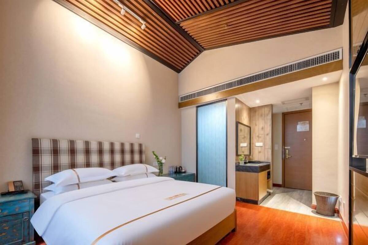 Quarto de hotel com uma cama grande, teto de madeira, banheiro com pia e porta que dá para outro quarto.
