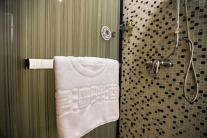 Une salle de bain avec un mur à rayures, une serviette blanche suspendue à un porte-serviettes et une douche ornée de motifs en mosaïque.