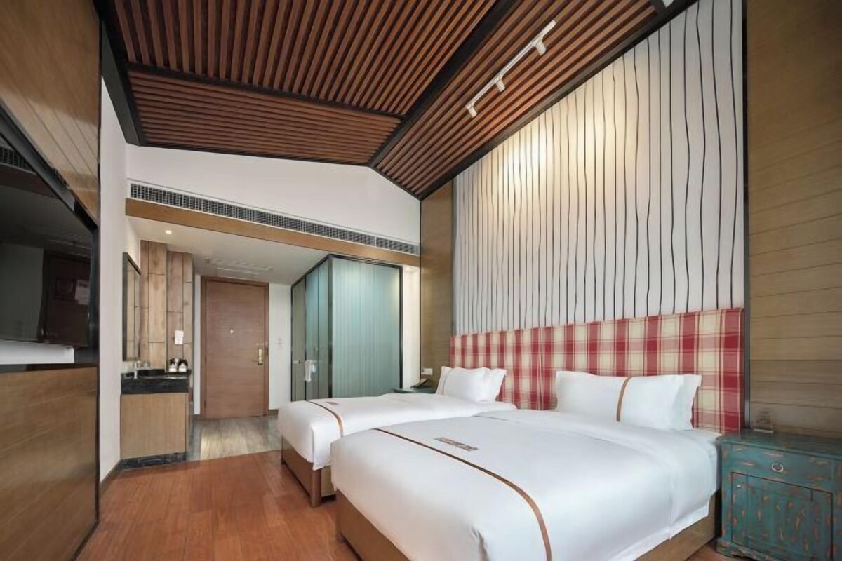Una habitación de hotel con dos camas, techo de madera, cabecero a cuadros y un mueble pequeño.