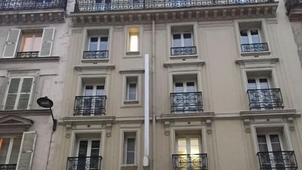 Un immeuble à plusieurs étages, doté de balcons, de grandes fenêtres et d’une enseigne indiquant la présence d’un commerce au rez-de-chaussée.