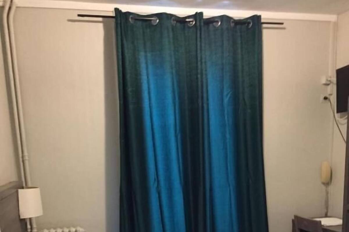 Ein Hotelzimmer mit Bett, Heizkörper, Schreibtisch und Stuhl sowie einem Vorhang.