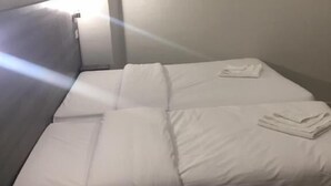 Un lit simple avec une literie blanche, dans une pièce dotée d’un plancher en bois et d’un mur blanc.