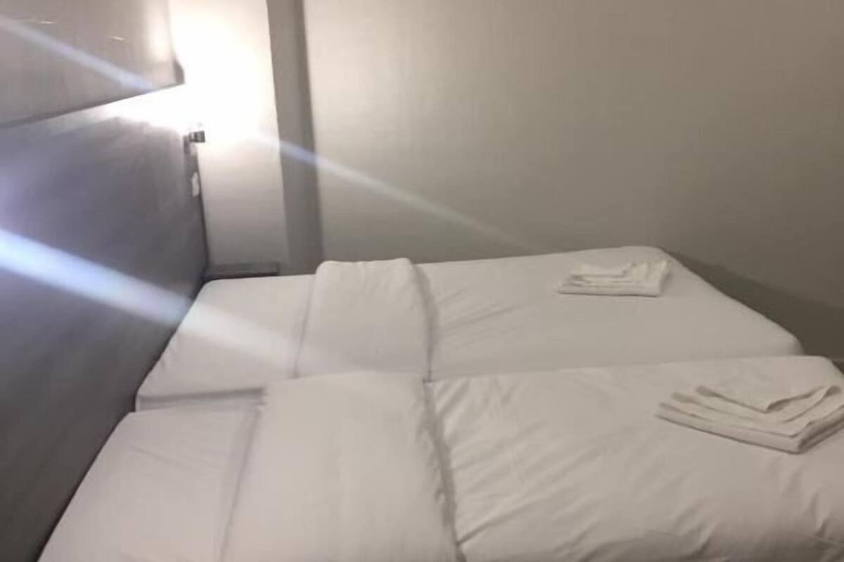 Ein Einzelbett mit weißer Bettwäsche in einem Zimmer mit Holzboden und weißer Wand.