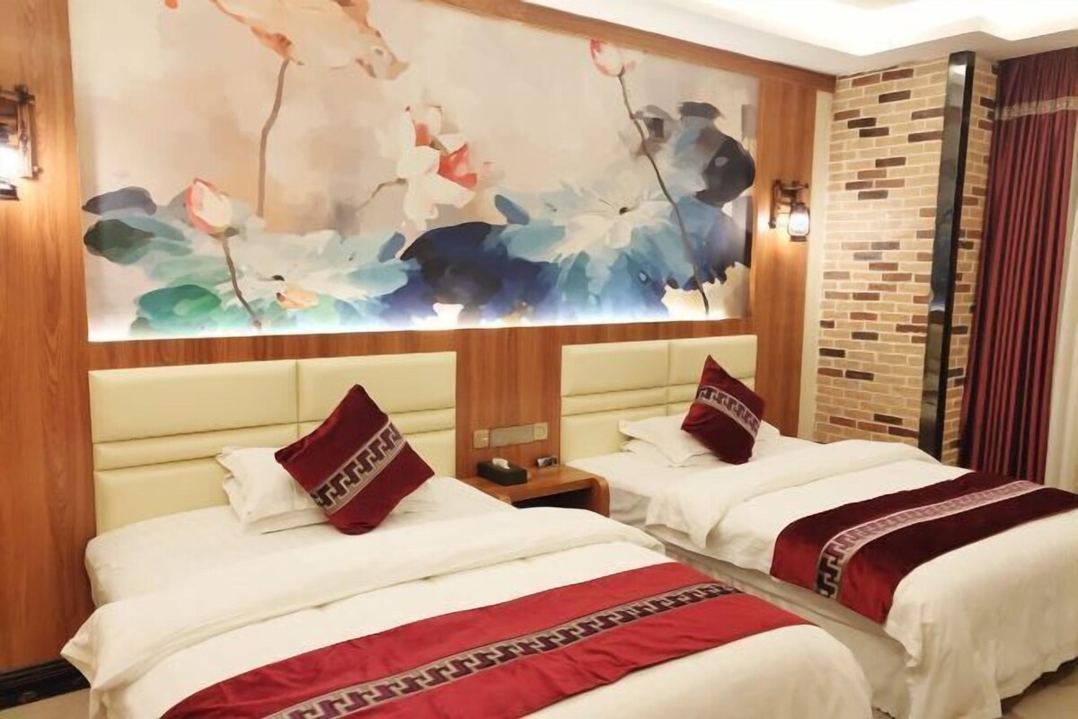 A hotel room with two beds, each with white bedding and red accents, a large floral artwork on the wall, and a brick accent wall.