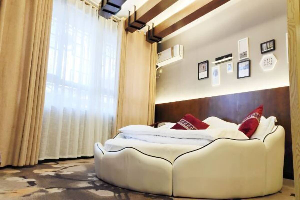 A round bed with white bedding and red pillows, a wooden headboard, and a wall-mounted air conditioner.