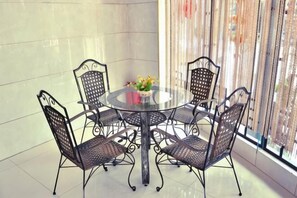 A round table with four chairs, a vase with flowers, and a view through a window with curtains. - Shengcheng Jiayuan Hotel (Leishan)