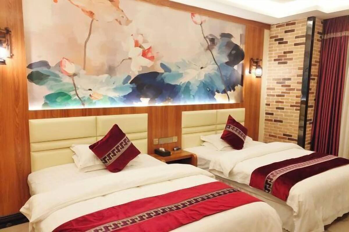 A hotel room with two beds, a large floral artwork on the wall, a brick accent wall, and a nightstand with a lamp.