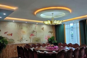 A dining area with a round table, chairs, a chandelier, and a wall with floral artwork. - Shengcheng Jiayuan Hotel (Leishan)