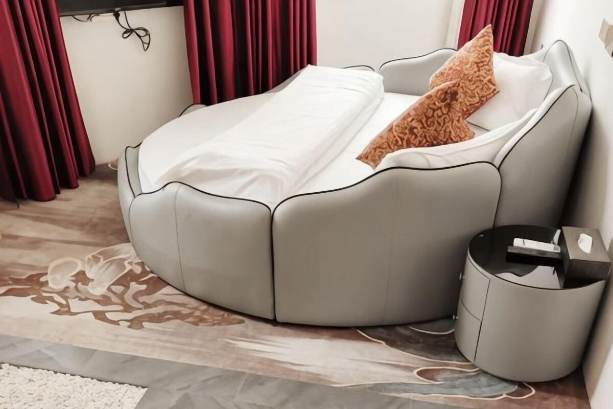 A modern, curved sofa bed with a white cover and a brown pillow, positioned next to a black side table with a remote control.