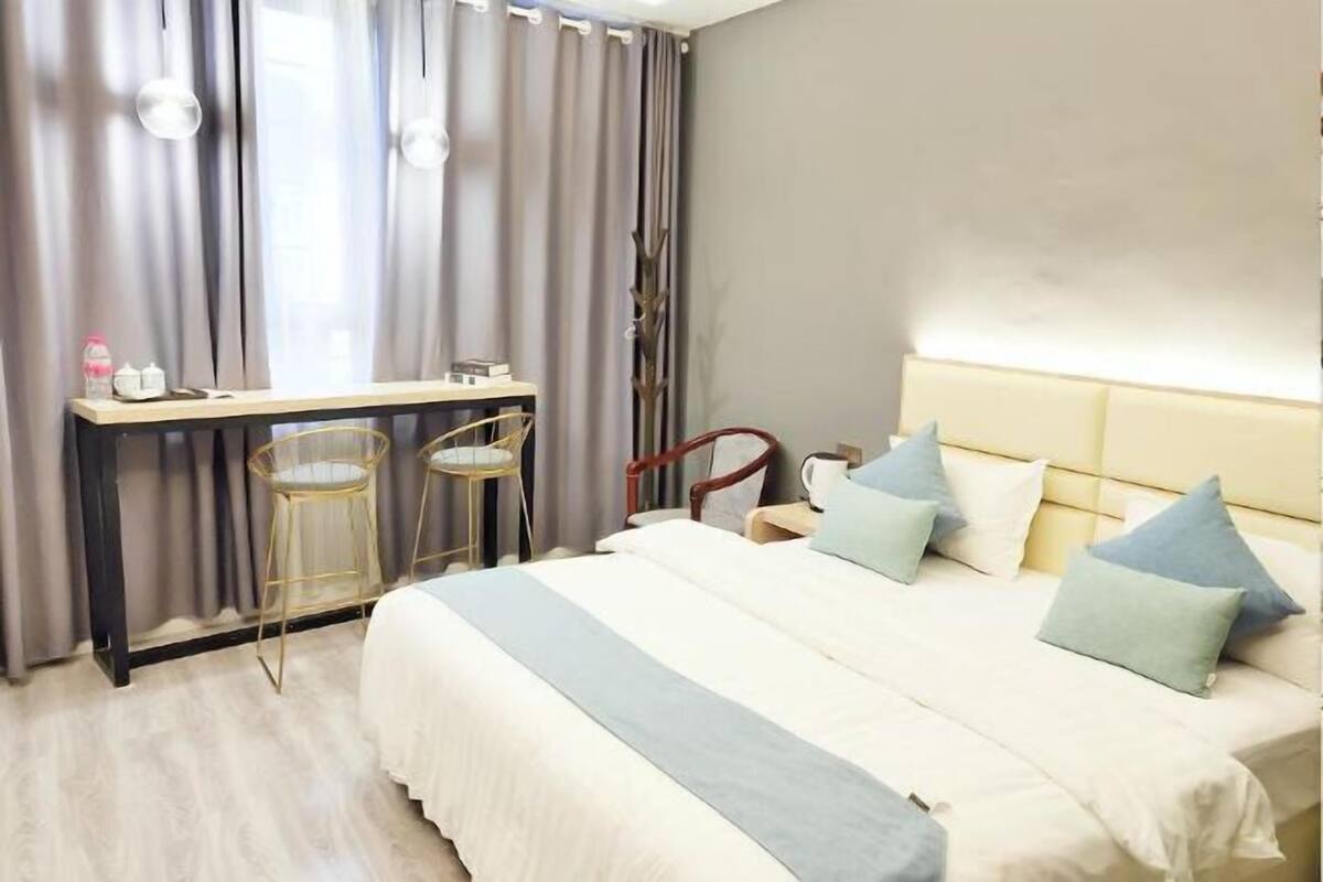 A hotel room with a bed, bedside tables, a mirror, and a window with curtains.