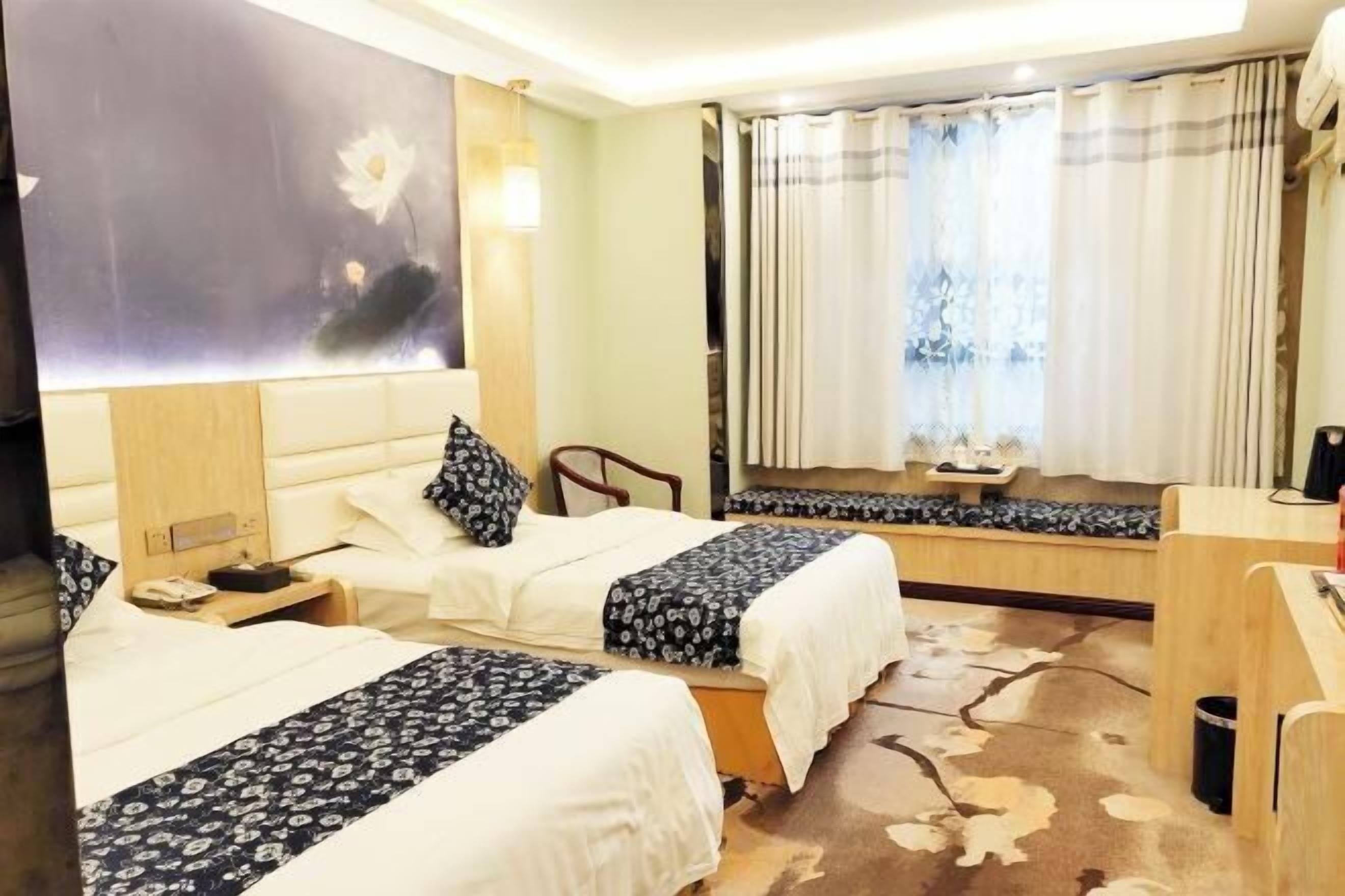 Quarto de hotel com duas camas, um quadro grande na parede, uma escrivaninha e uma janela com cortinas.