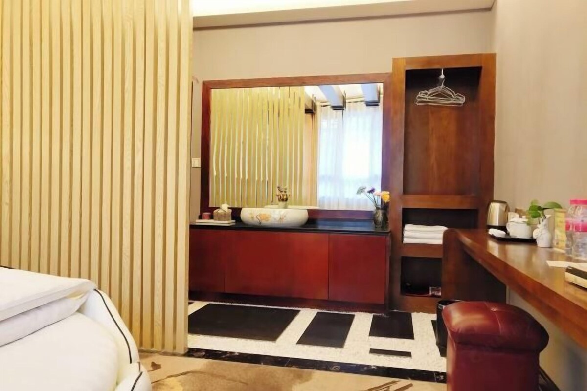 A hotel room with a bed, a wooden vanity with a mirror, a sink, and a red chair.