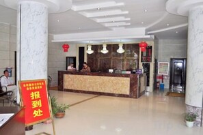 Un hall d’hôtel avec un comptoir de réception en marbre, un panneau rouge et quelques personnes.