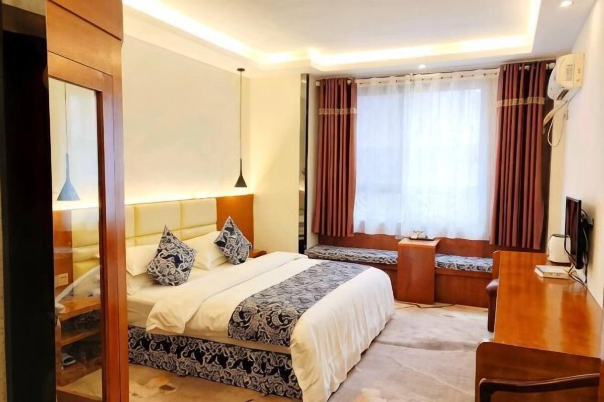 A hotel room with a bed, bedside table, chair, and a desk with a chair.