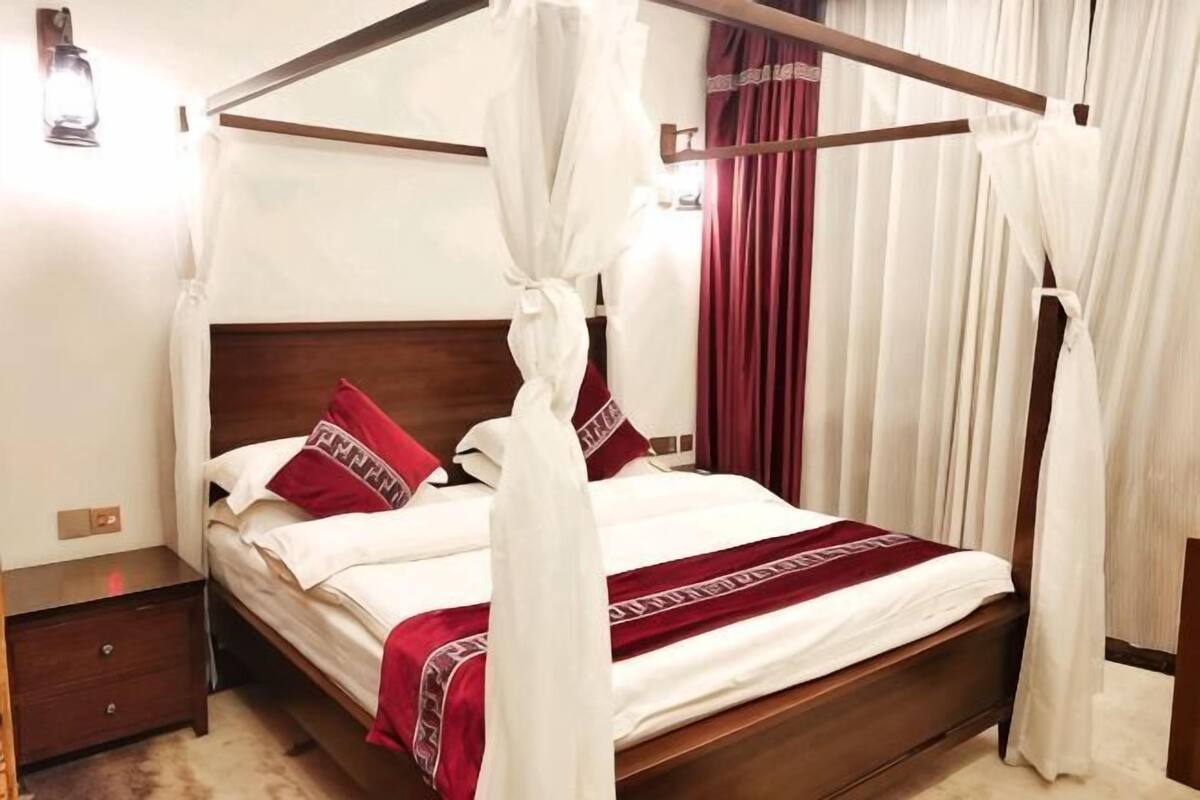 A four-poster bed with a canopy, a wooden headboard, and a red and white bedspread.