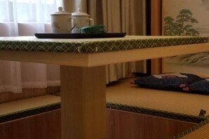 Una habitación con tatami, una mesa de madera baja, un cojín verde y una bandeja con tetera y tazas.