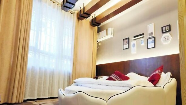 A modern bedroom with a curved bed, beige curtains, and framed pictures on the wall. - Shengcheng Jiayuan Hotel (Leishan)