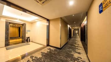 Pasillo de hotel con suelo alfombrado, zona de recepción con puerta de vidrio y un letrero que indica el número de habitación.