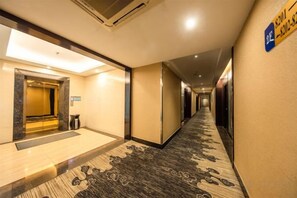 A hotel corridor with a carpeted floor, a reception area with a glass door, and a sign indicating the room number. - Park Lane Yiju Hotel (Jiangmen Taishan Pedestrian Street Pinghu Road) (Taishan)