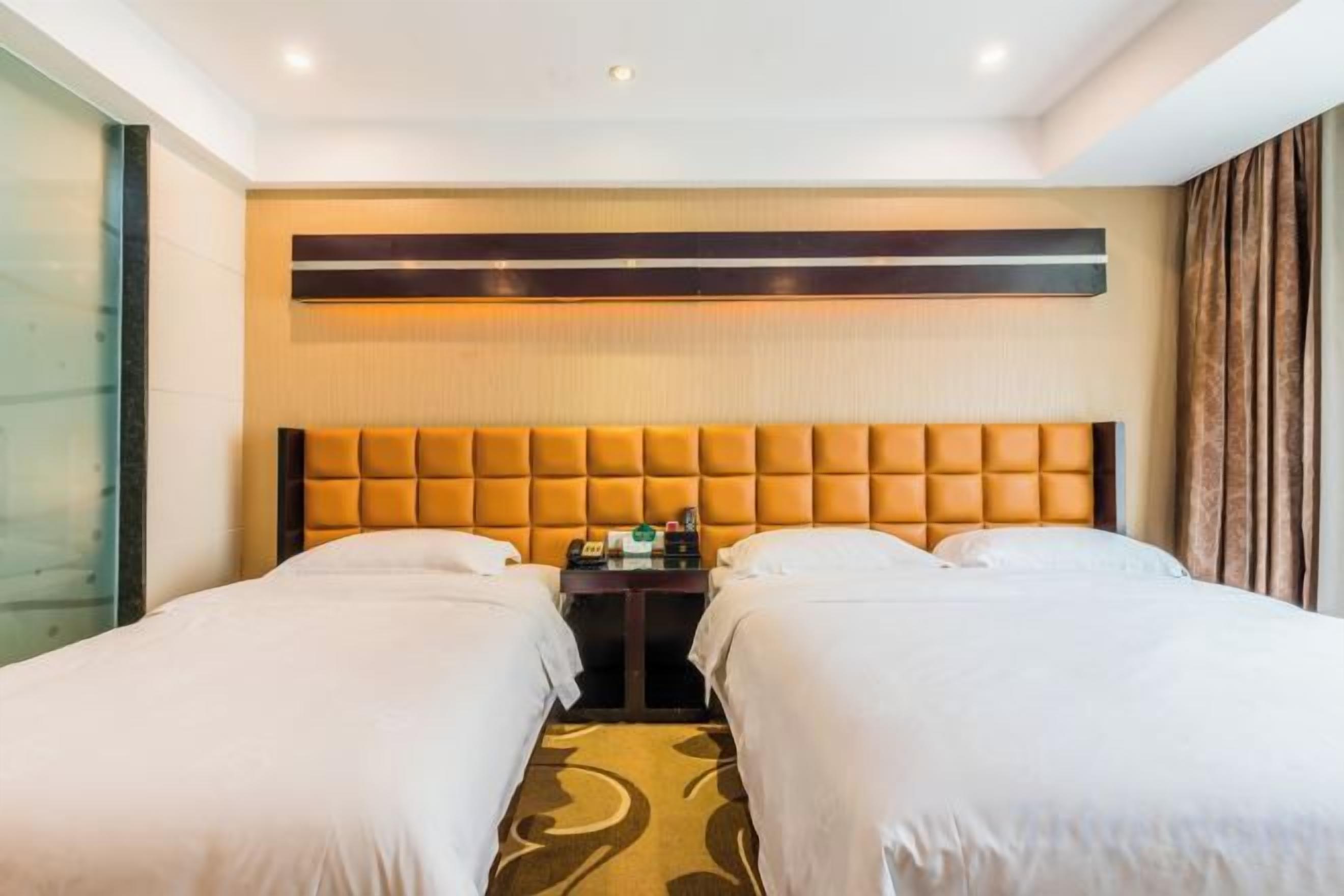Ein Hotelzimmer mit zwei Betten, einem Kopfteil, einem Nachttisch und einem Fenster mit Vorhängen.