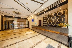 A hotel reception area with a marble floor, a reception desk with a geometric patterned wall, and a glass door entrance. - Park Lane Yiju Hotel (Jiangmen Taishan Pedestrian Street Pinghu Road) (Taishan)