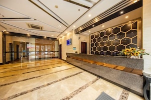 A hotel reception area with a marble floor, a reception desk with a geometric patterned wall, and a glass door entrance.