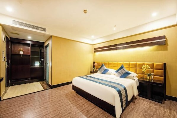 Una habitación de hotel con cama, mesitas de noche, cabecera y puerta que da a un baño.