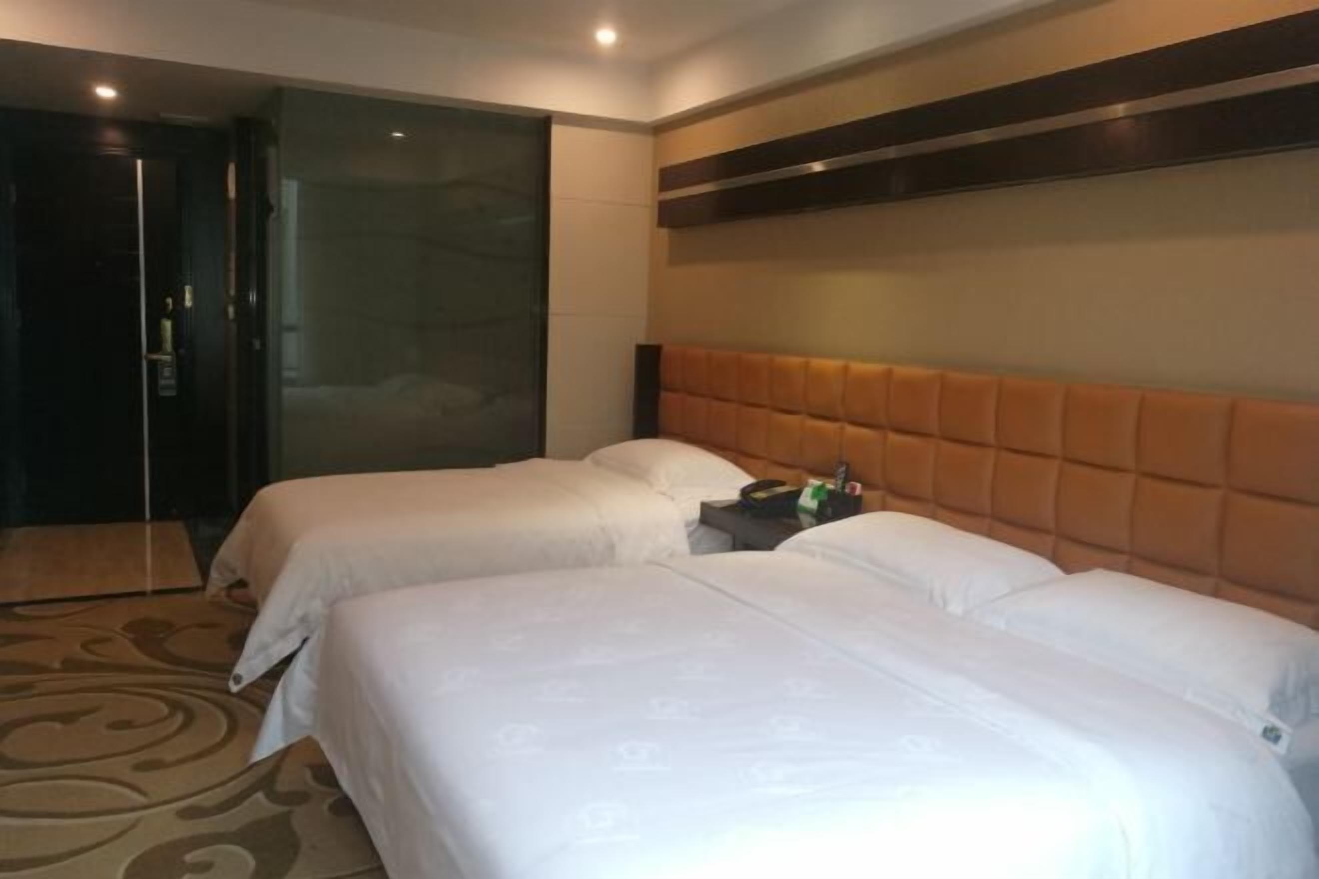 Habitación de hotel con dos camas, una puerta de vidrio que da a la zona de la ducha y un cabecero de madera.