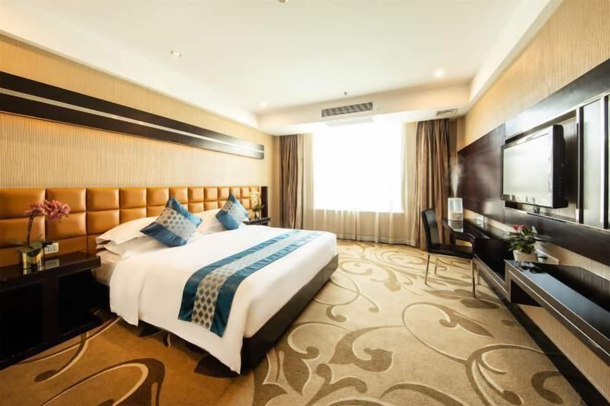 A hotel room with a large bed, a flat-screen TV, a desk, and a large window.