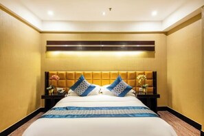A hotel room with a large bed, a headboard with a light fixture, and two bedside tables with floral arrangements. - Park Lane Yiju Hotel (Jiangmen Taishan Pedestrian Street Pinghu Road) (Taishan)