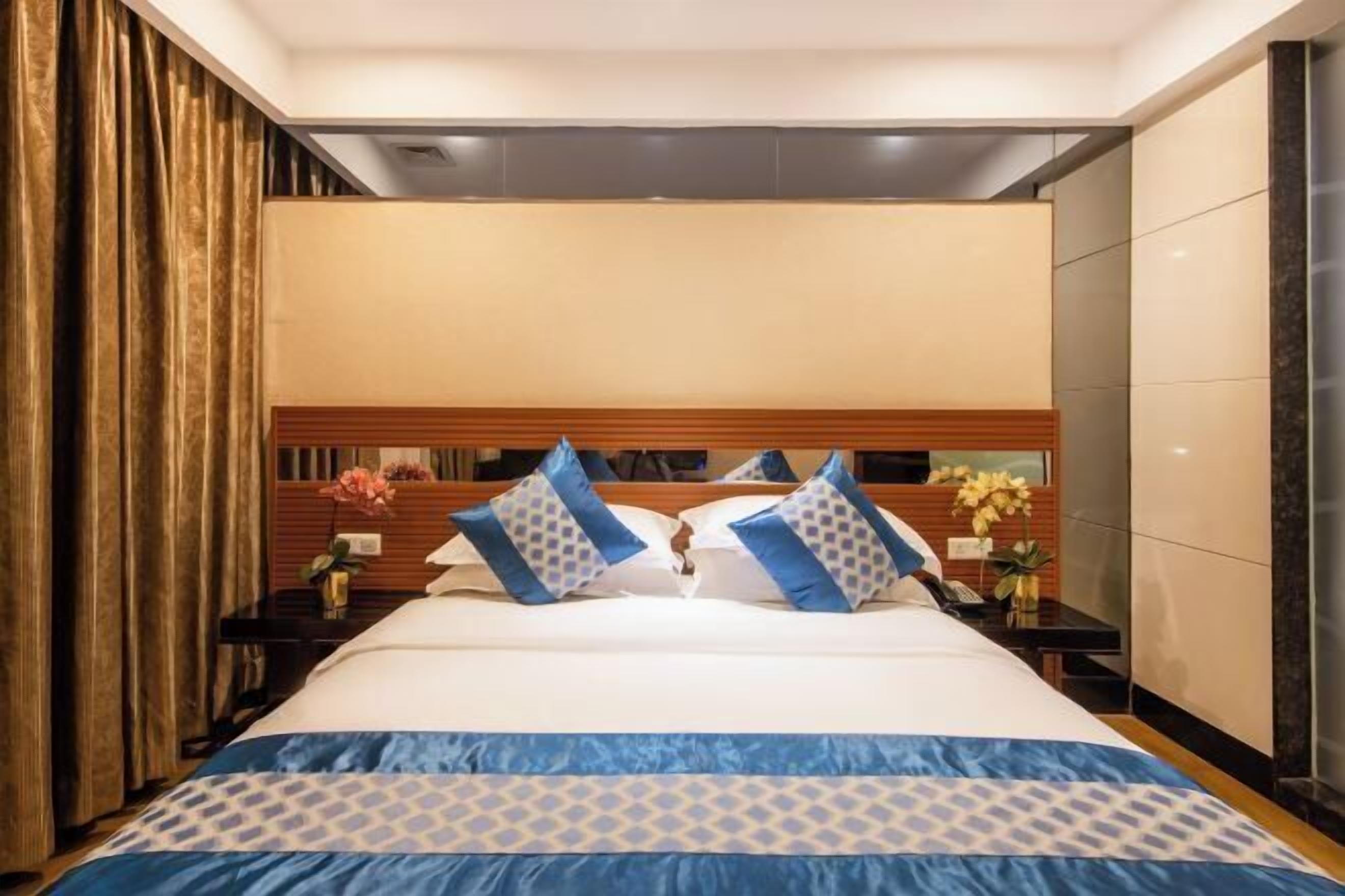 A hotel room with a large bed, a wooden headboard, and a nightstand with a lamp and flowers.