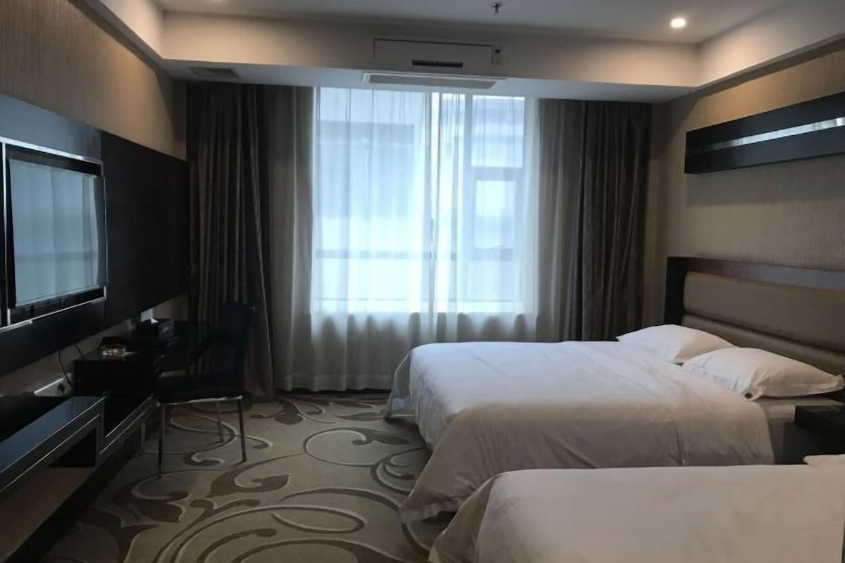 Una habitación de hotel con dos camas, televisión, escritorio y ventana con cortinas.